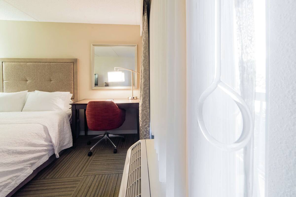 A hotel room with a bed, a desk, a chair, a mirror, and a window with curtains.