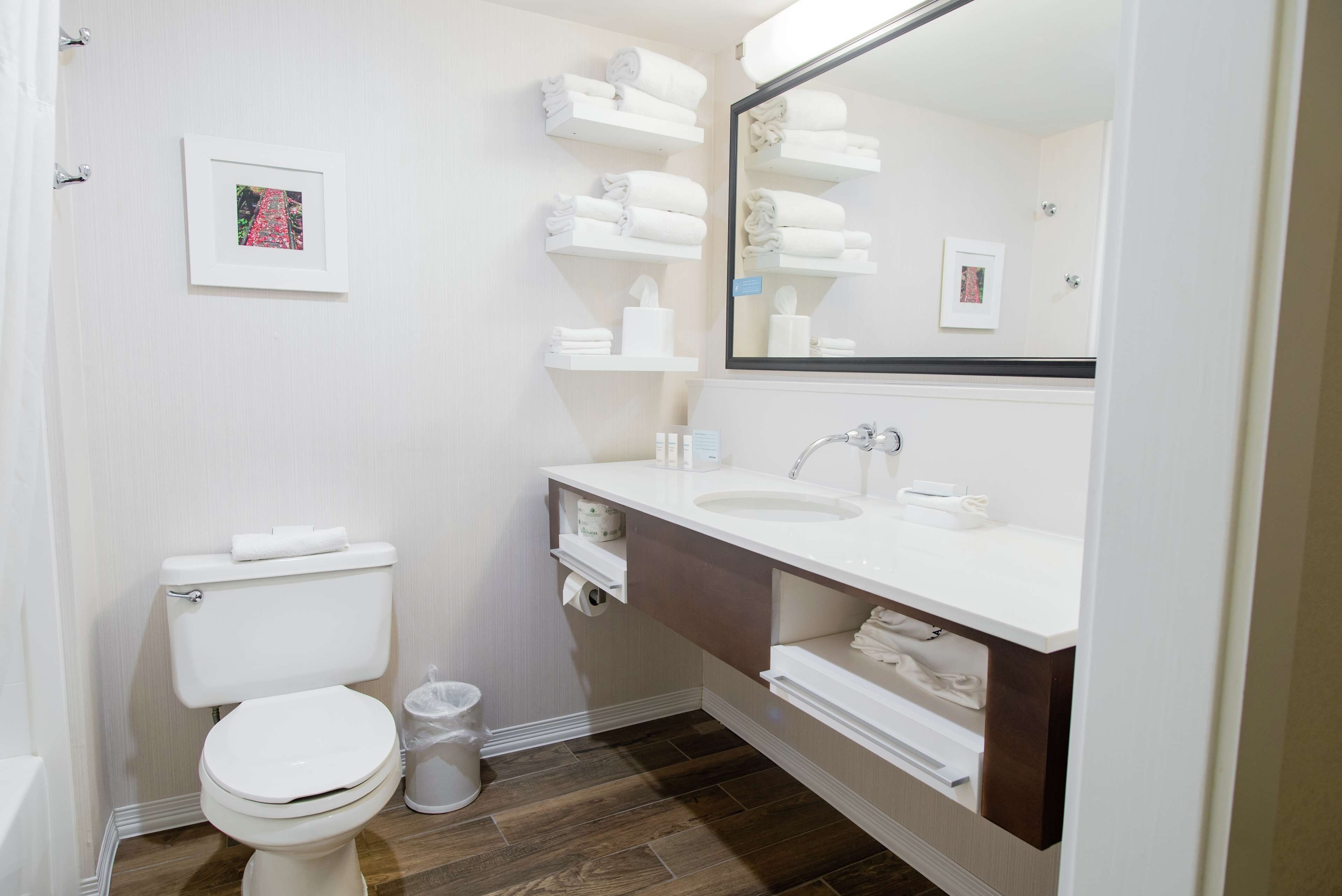 A bathroom with a toilet, sink, mirror, and shelves with towels.