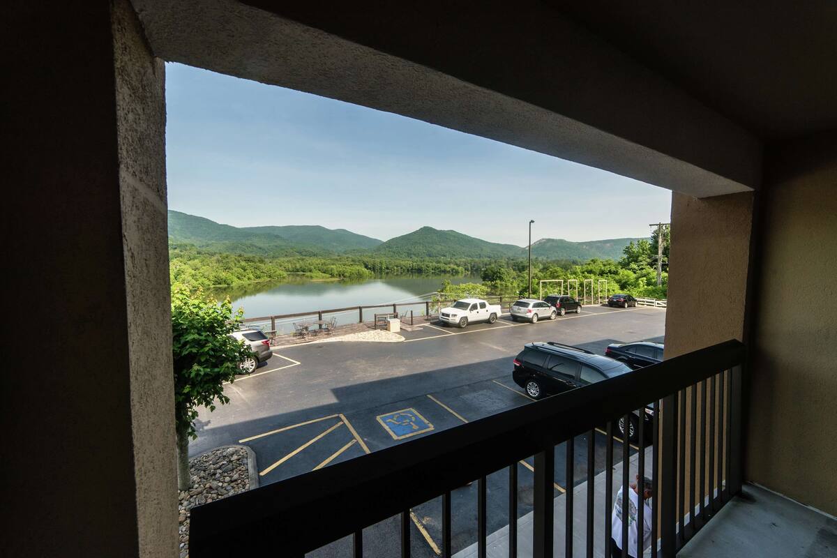 A view from a balcony overlooking a parking area with a lake and mountains in the background.
