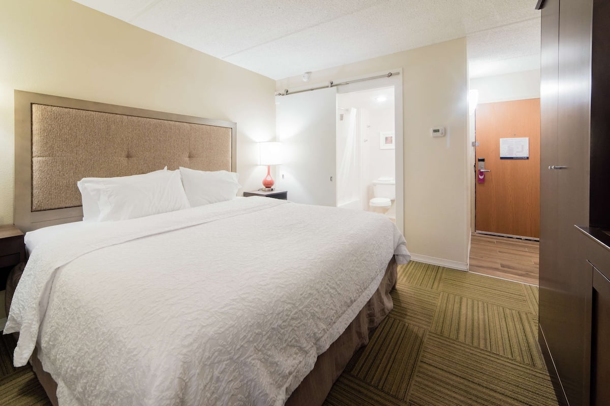 A hotel room with a large bed, a nightstand with a lamp, a wooden door, and a shower area.