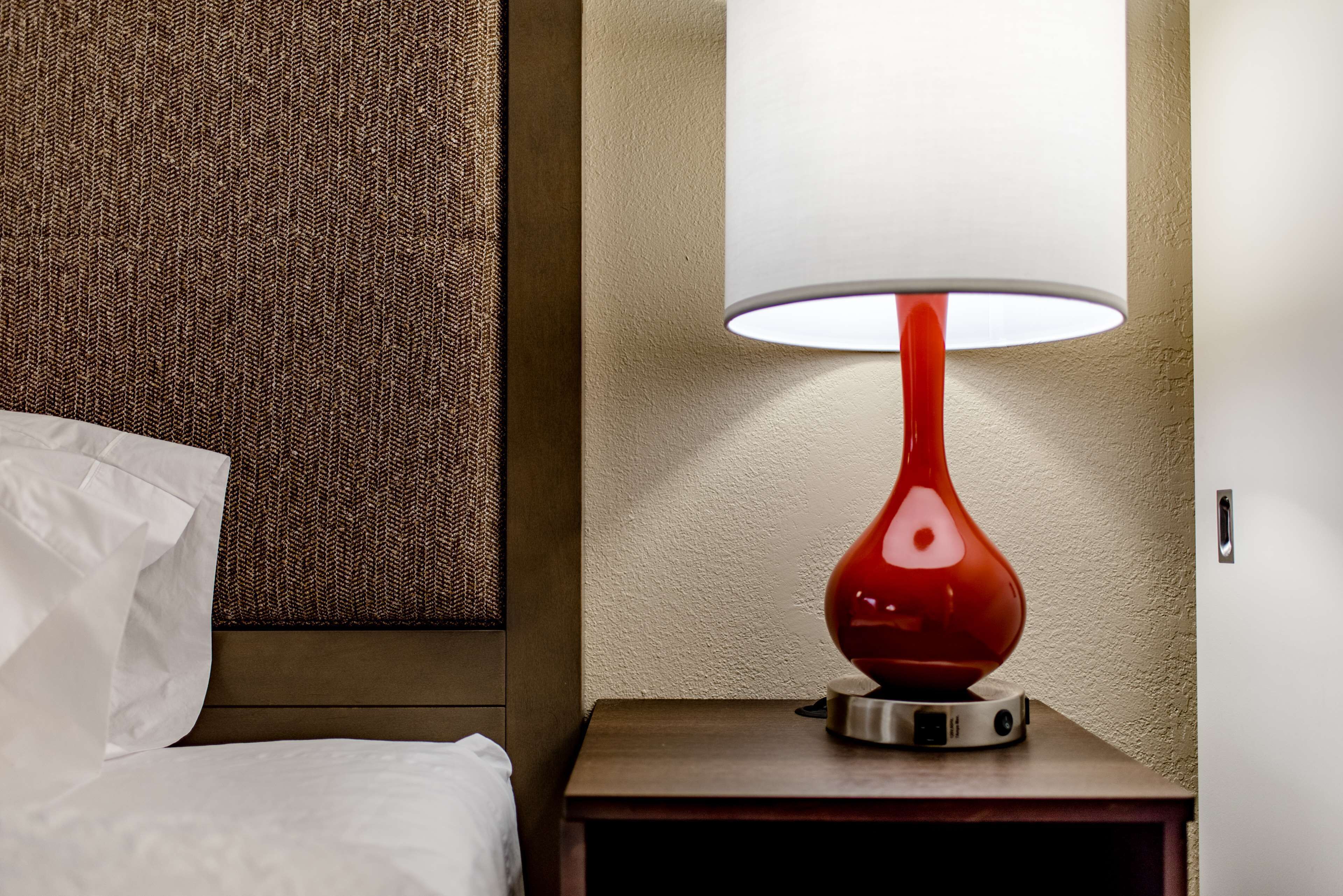 A hotel room with a bed, a red table lamp, and a textured wall.