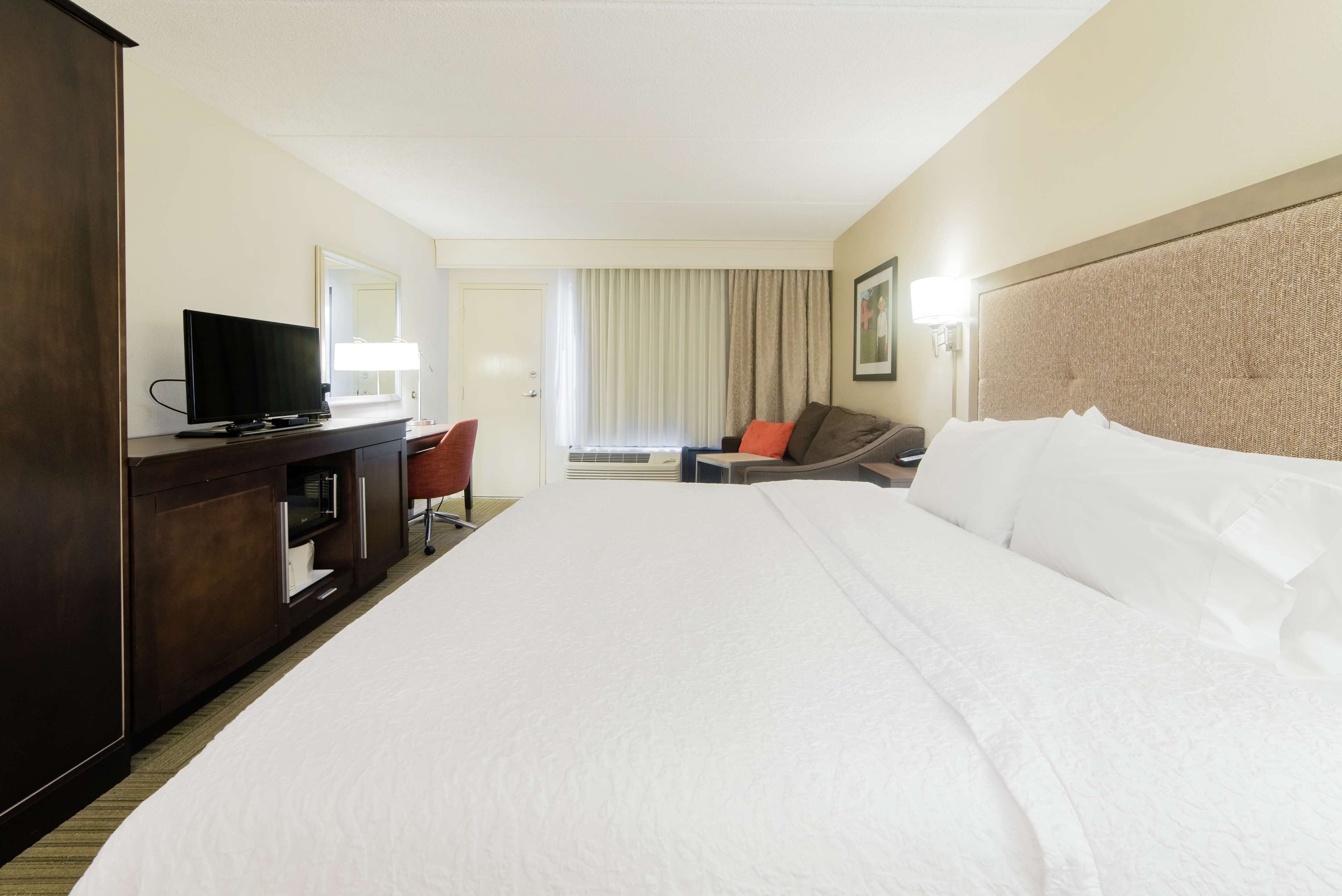A hotel room with a large bed, a desk with a television, a chair, and a sofa.