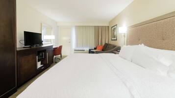 A hotel room with a large bed, a desk with a television, a chair, and a sofa.