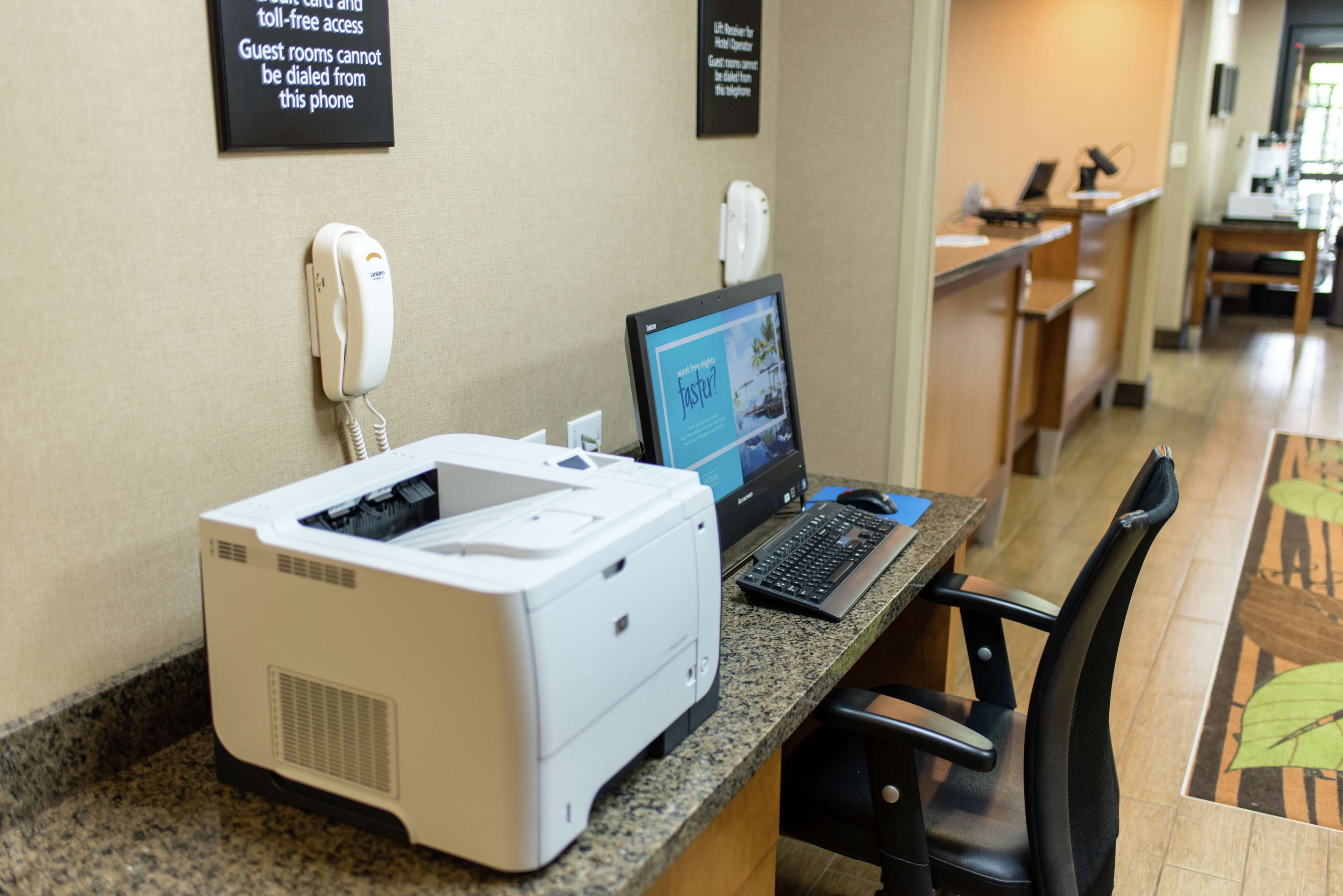 A hotel reception area with a desktop computer, a printer, and a phone on a counter.
