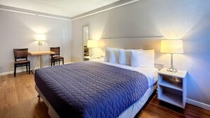Habitación de hotel con una cama grande, dos mesitas de noche con lámparas, un escritorio pequeño con silla y suelo de madera.