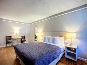 Une chambre d’hôtel avec un grand lit, deux tables de chevet avec des lampes, un petit bureau avec une chaise et un plancher en bois.
