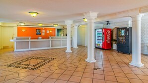 Un vestíbulo con mostrador de recepción, máquinas expendedoras de Coca-Cola y suelo de baldosas.