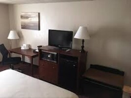 A hotel room with a bed, a desk, a television, and two lamps.
