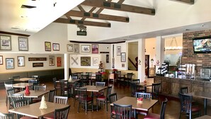 Un restaurant avec des tables et des chaises en bois, des tableaux encadrés aux murs et une cheminée en briques.