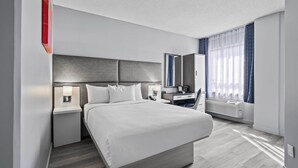 A modern hotel room with a large bed, bedside tables with lamps, a desk, a chair, a mirror, and a window with curtains. - Travelodge Hotel by Wyndham Montreal Centre (Montreal)