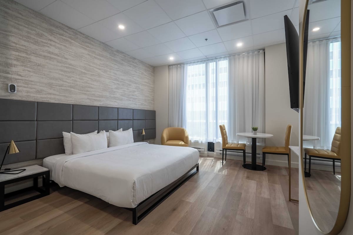 A modern hotel room with a large bed, a sofa, a small table, and a TV.