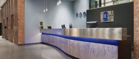 Zona de recepción con diseño moderno, que incluye un mostrador curvo, una pared azul decorativa y una pared de ladrillo en un lateral.