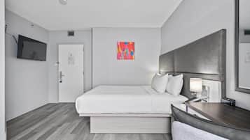 A hotel room with a bed, bedside table, lamp, and a television on the wall.