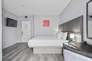 A hotel room with a bed, bedside table, lamp, and a television on the wall.