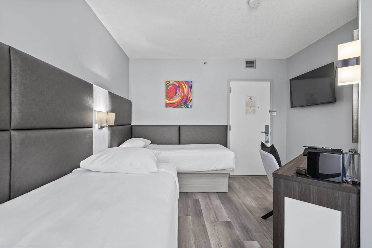A hotel room with two beds, a desk, a TV, and a colorful artwork on the wall.