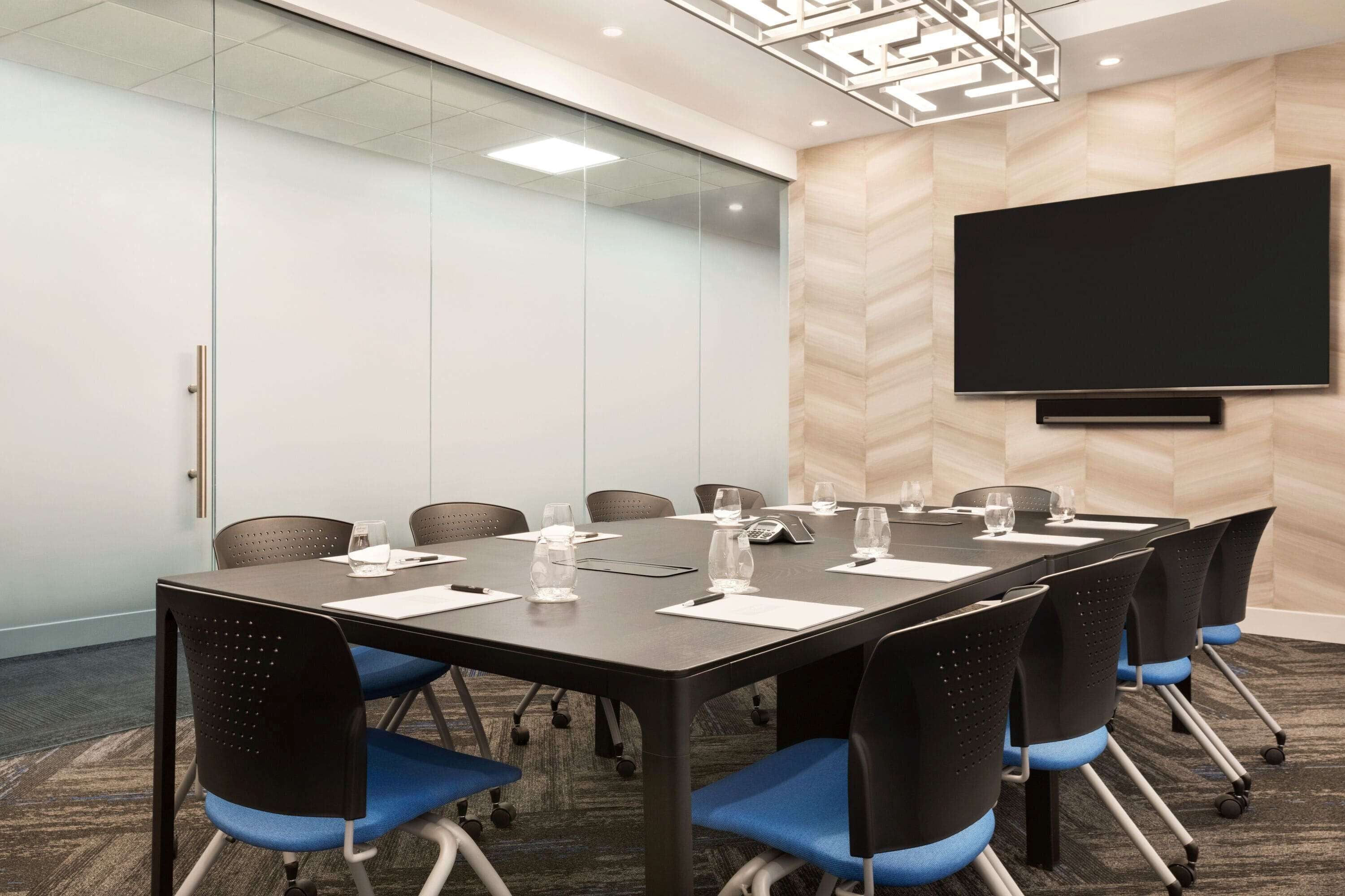 A conference room with a large table, chairs, a flat-screen TV, and a glass partition wall.