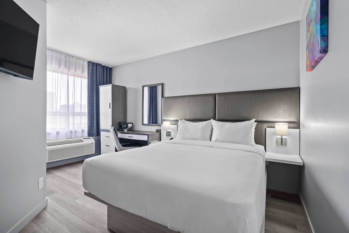 A hotel room with a large bed, bedside tables, a desk, a chair, a flat-screen TV, and a window with curtains.