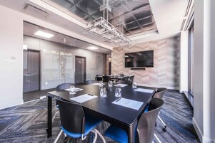A conference room with a large table, chairs, a flat-screen TV, and a glass partition wall.