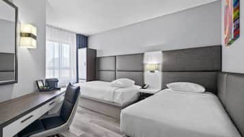 A hotel room with two beds, a desk, a chair, a desk lamp, a phone, and a painting on the wall.