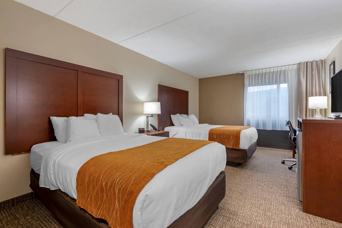 Una habitación de hotel con dos camas, un escritorio, un televisor y una ventana con cortinas.