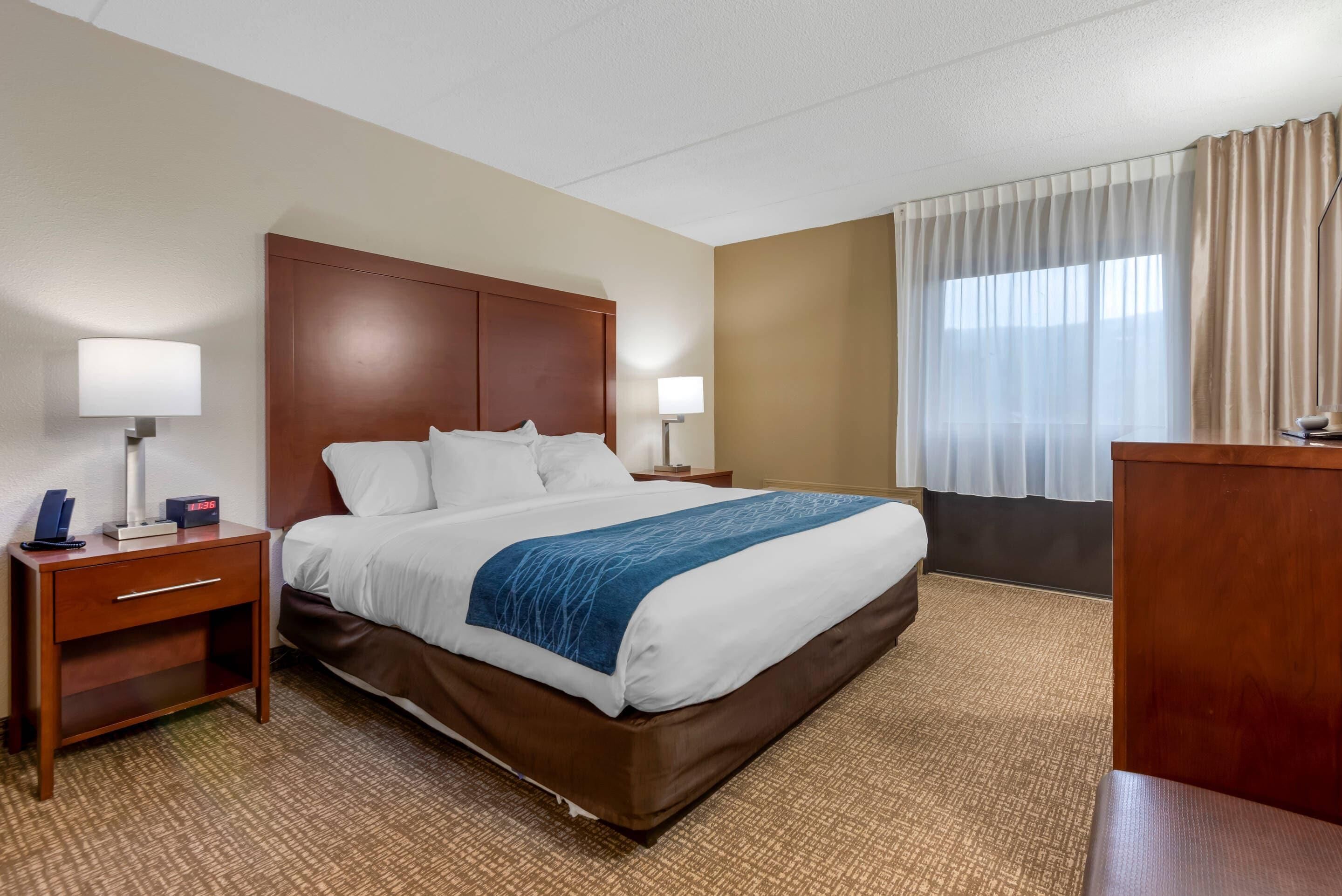 A hotel room with a bed, bedside tables, lamps, a desk, and a window with curtains.