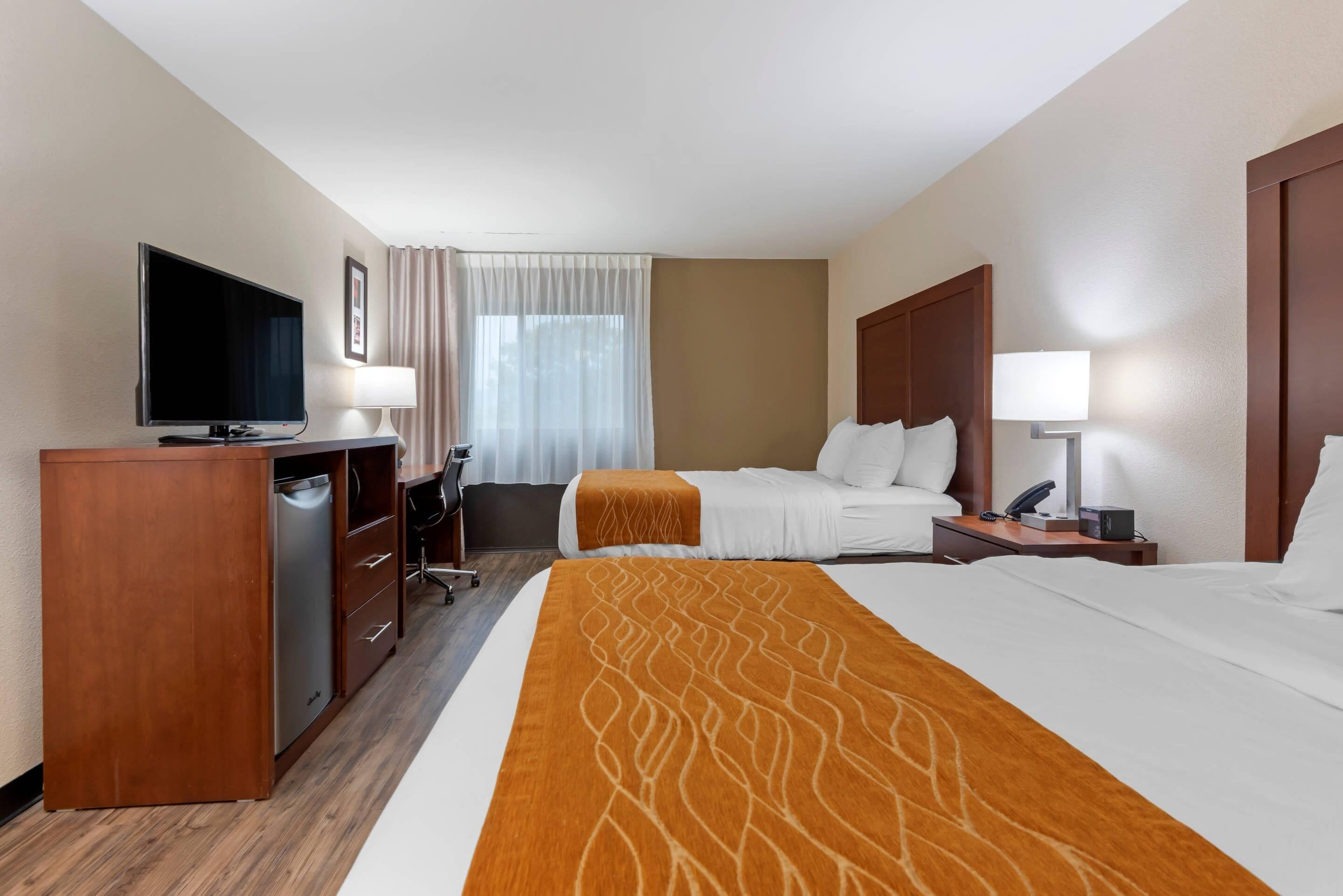 Een hotelkamer met een bed, een bureau met televisie, een stoel, een nachtkastje met lamp en een raam met gordijnen.