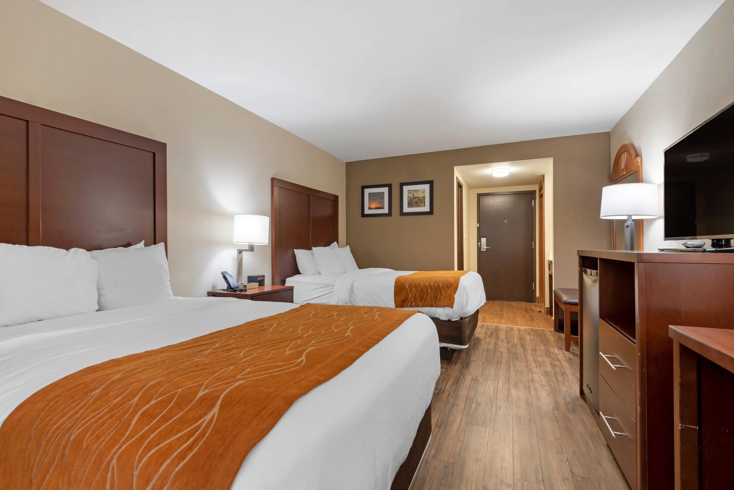 Habitación de hotel con dos camas, un escritorio, una silla, un televisor y una puerta que da a otra habitación.