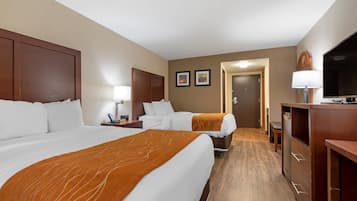 Habitación de hotel con dos camas, un escritorio, una silla, un televisor y una puerta que da a otra habitación.