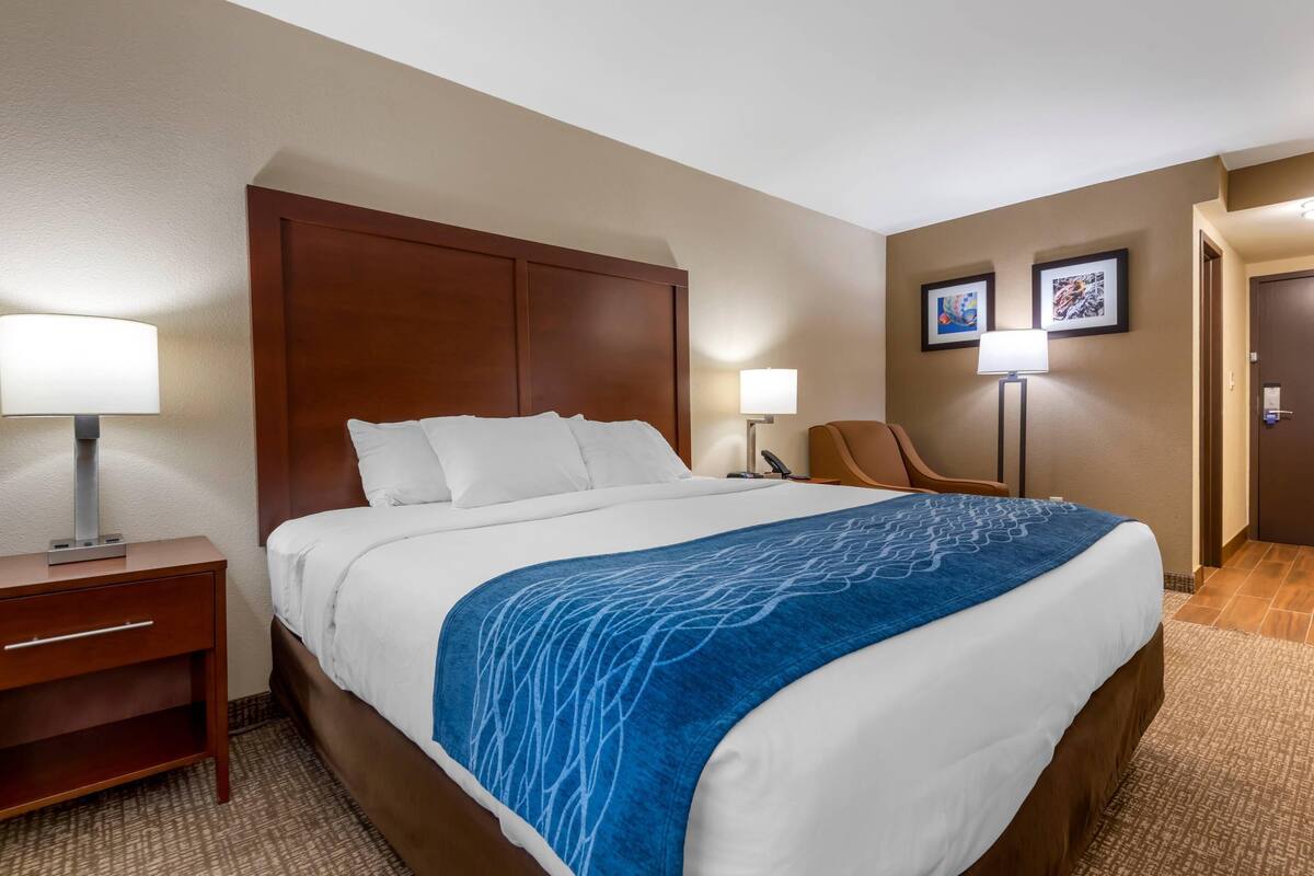 Habitación de hotel con una cama grande, una mesita de noche, una silla, dos lámparas de pared y cuadros enmarcados.