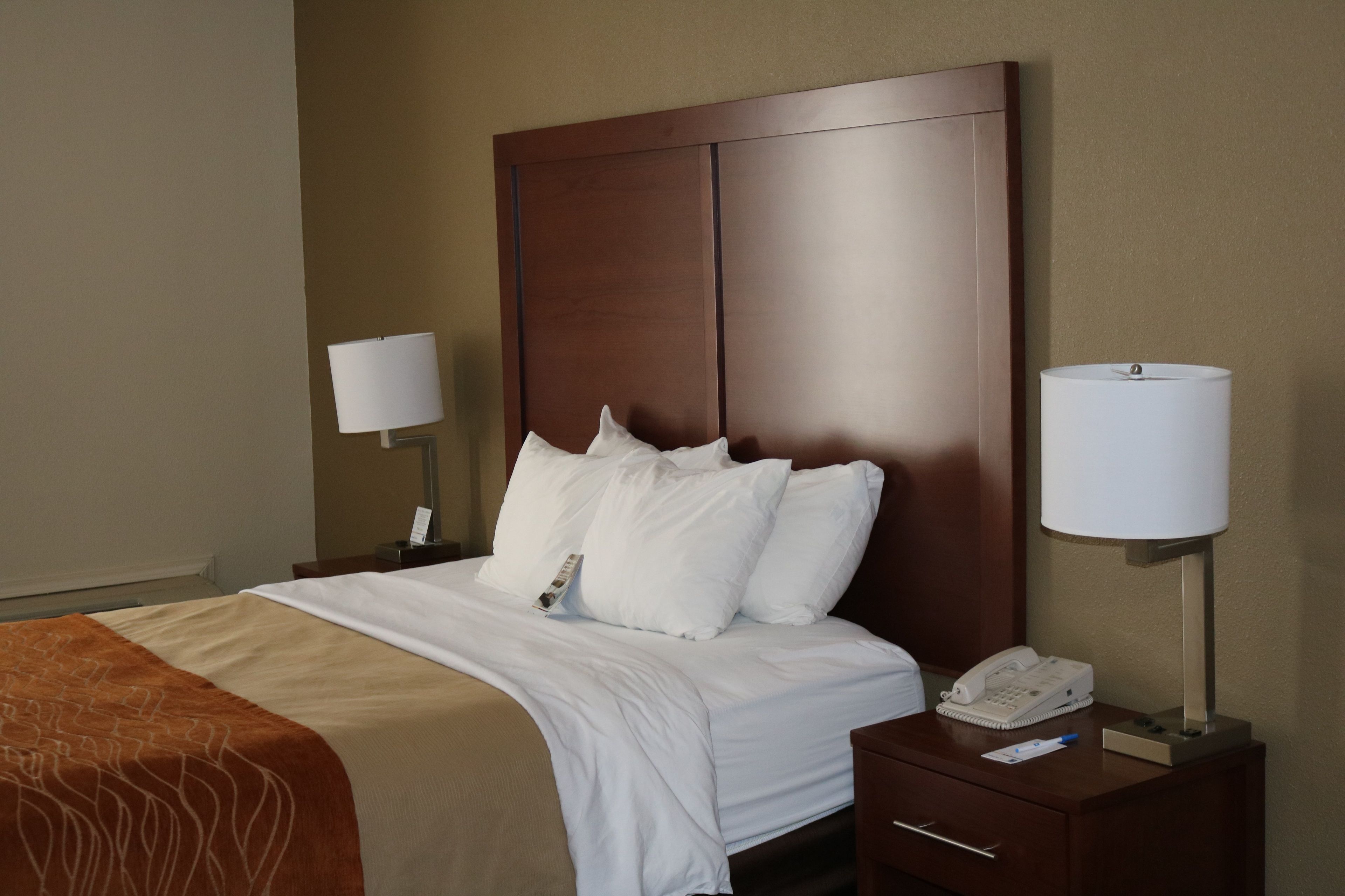 A hotel room with a large bed, two bedside tables, a nightstand, and a lamp.