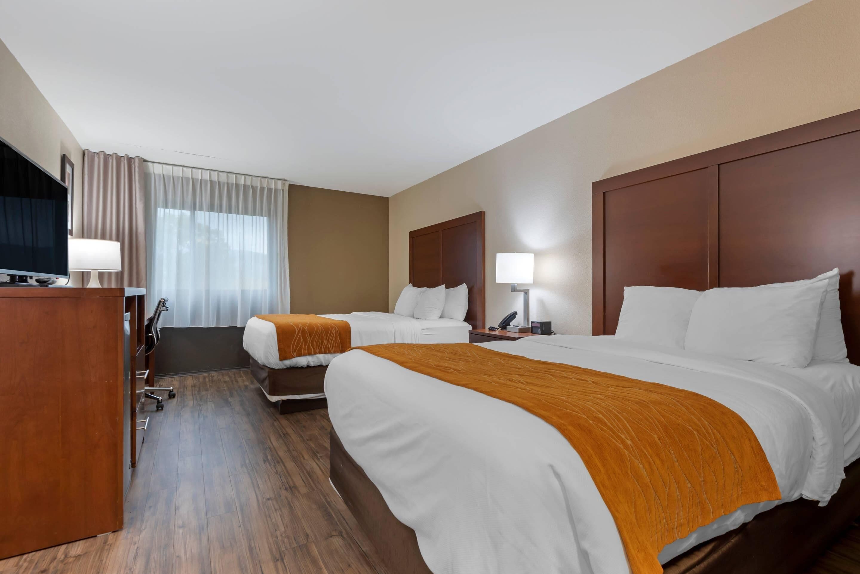 Habitación de hotel con dos camas, un escritorio, un televisor y una ventana con cortinas.