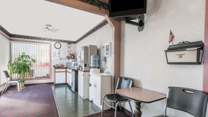 A compact kitchen with a microwave, refrigerator, and sink. There is a dining area with a table and chairs, and a potted plant in the corner. - Knights Inn Ottawa (Ottawa)
