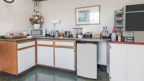 A compact kitchen with a microwave, toaster, and small refrigerator. There is a clock on the wall and a framed picture above the counter. - Knights Inn Ottawa (Ottawa)