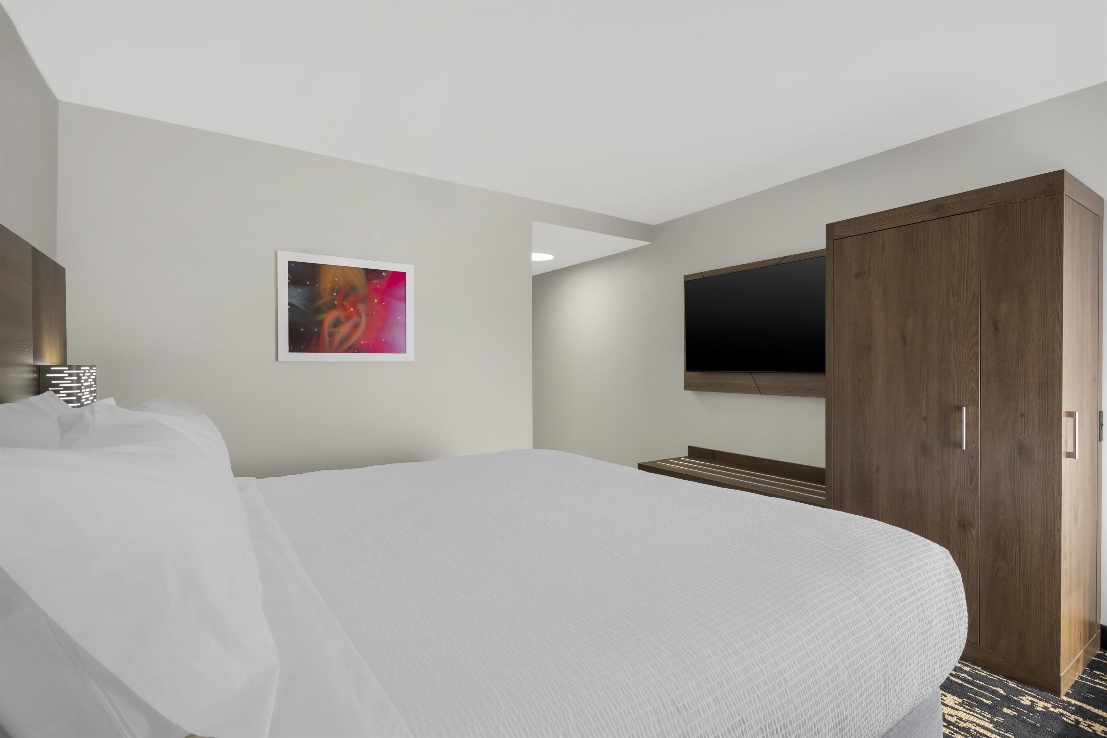 A hotel room with a bed, a wardrobe, a television, and a painting on the wall.