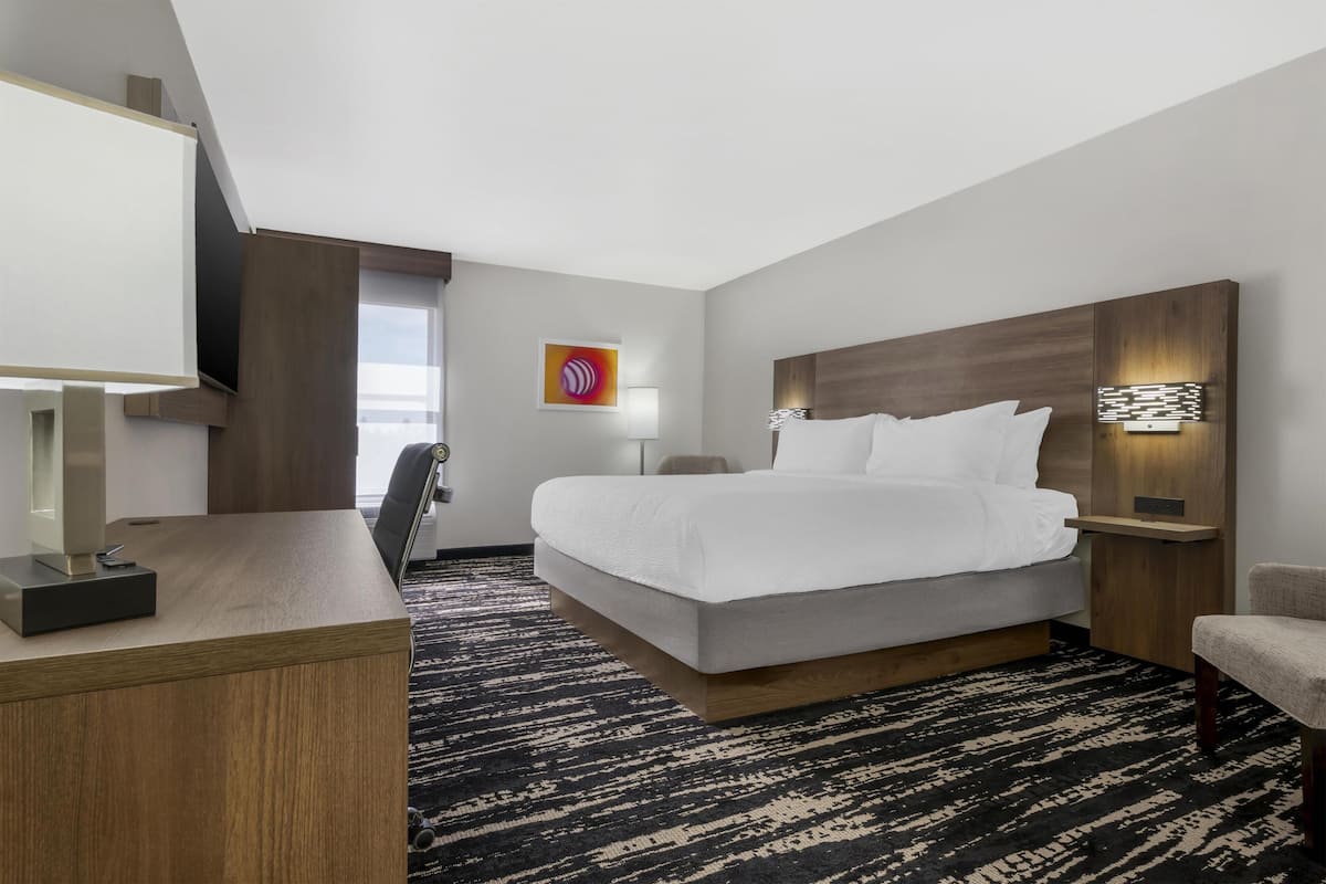 A hotel room with a bed, desk, chair, and a view of the outdoors.