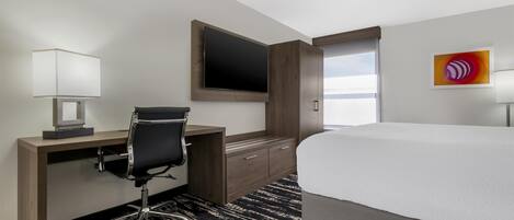 A hotel room with a bed, desk, chair, TV, and artwork on the wall.
