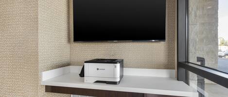 A flat-screen TV mounted on a wall above a white counter with a Lexmark printer on it.