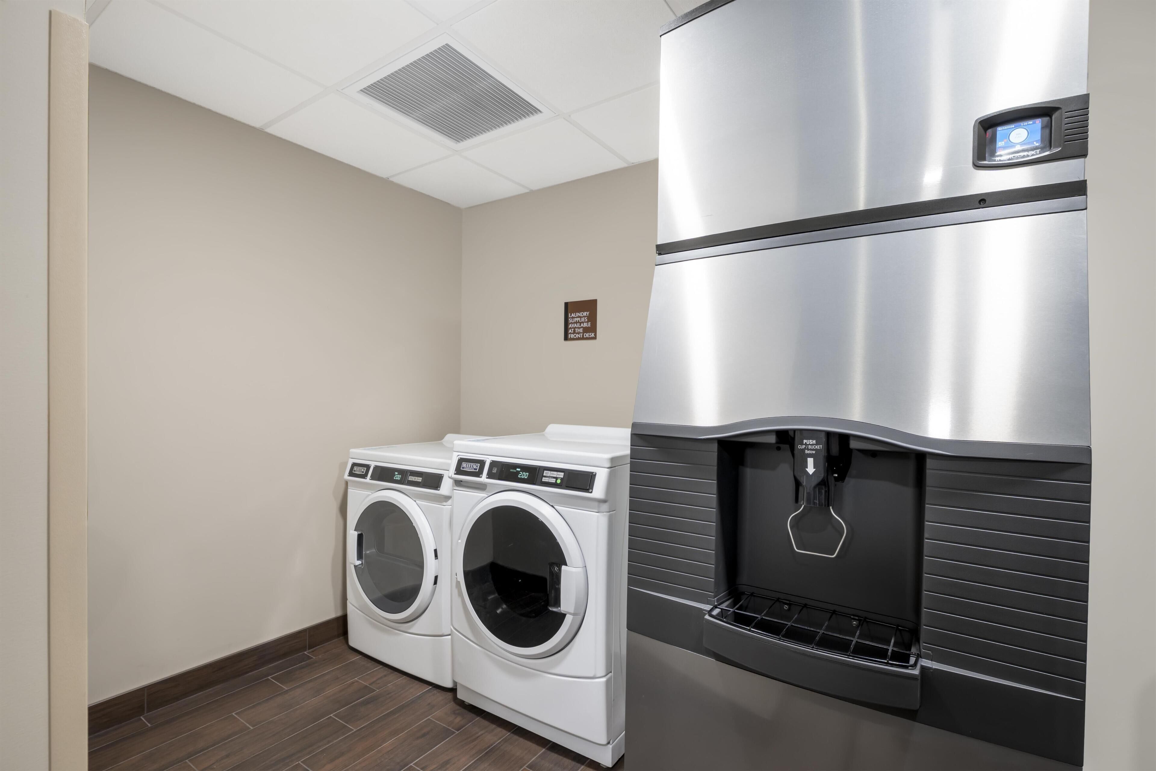 Un cuarto de lavandería con dos lavadoras de carga frontal y un refrigerador de acero inoxidable con dispensador de agua.