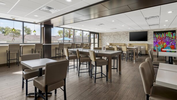 Un espace repas moderne, doté de tables et de chaises, de grandes fenêtres et d’un téléviseur à écran plat fixé au mur.