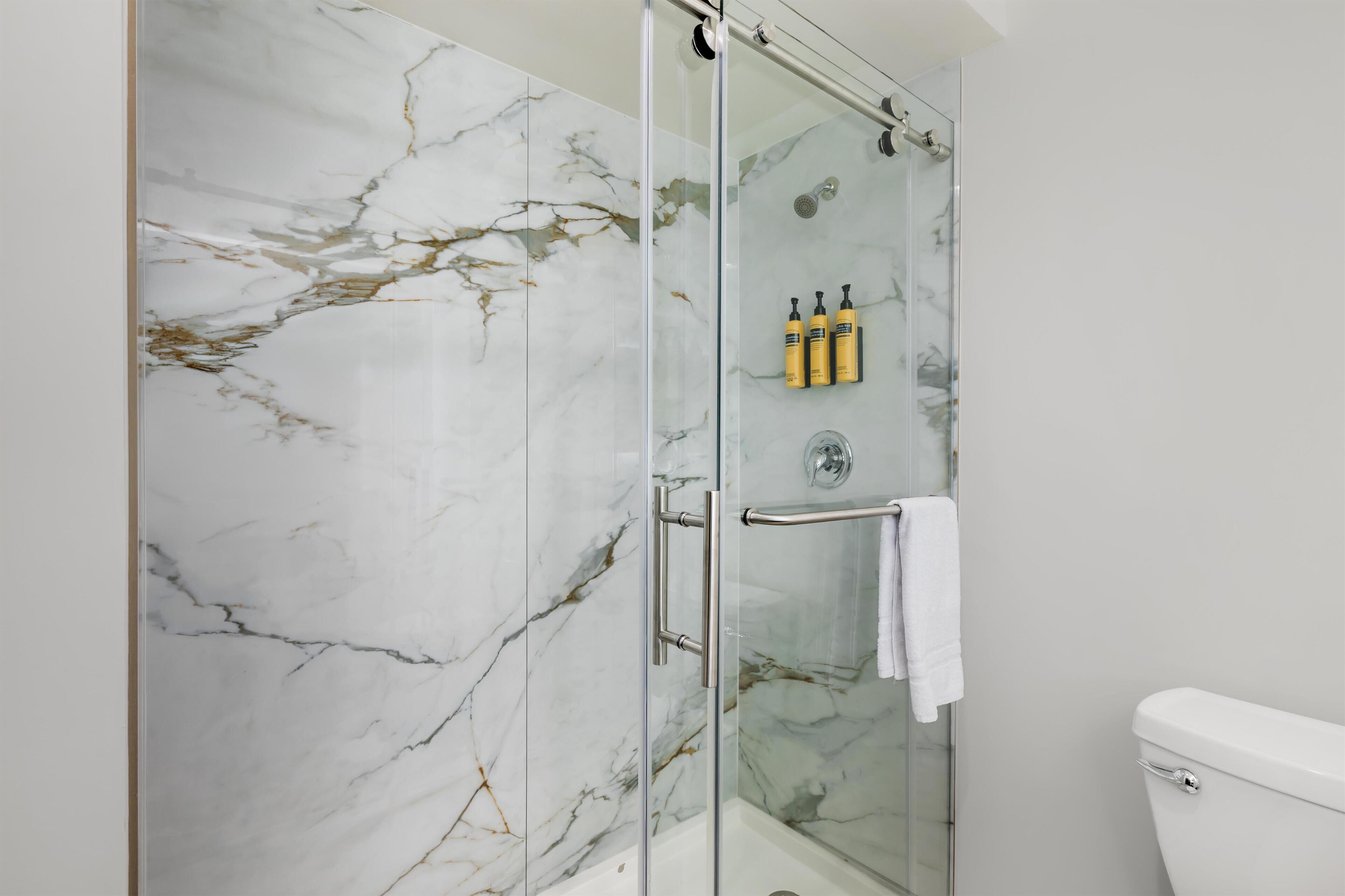 A bathroom with a glass-enclosed shower, marble walls, and a white toilet.