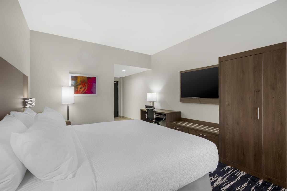 A hotel room with a large bed, a desk, a chair, a TV mounted on the wall, and a wardrobe.
