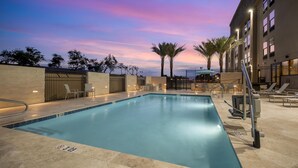 Une piscine avec une terrasse carrelée, des chaises longues et des palmiers.