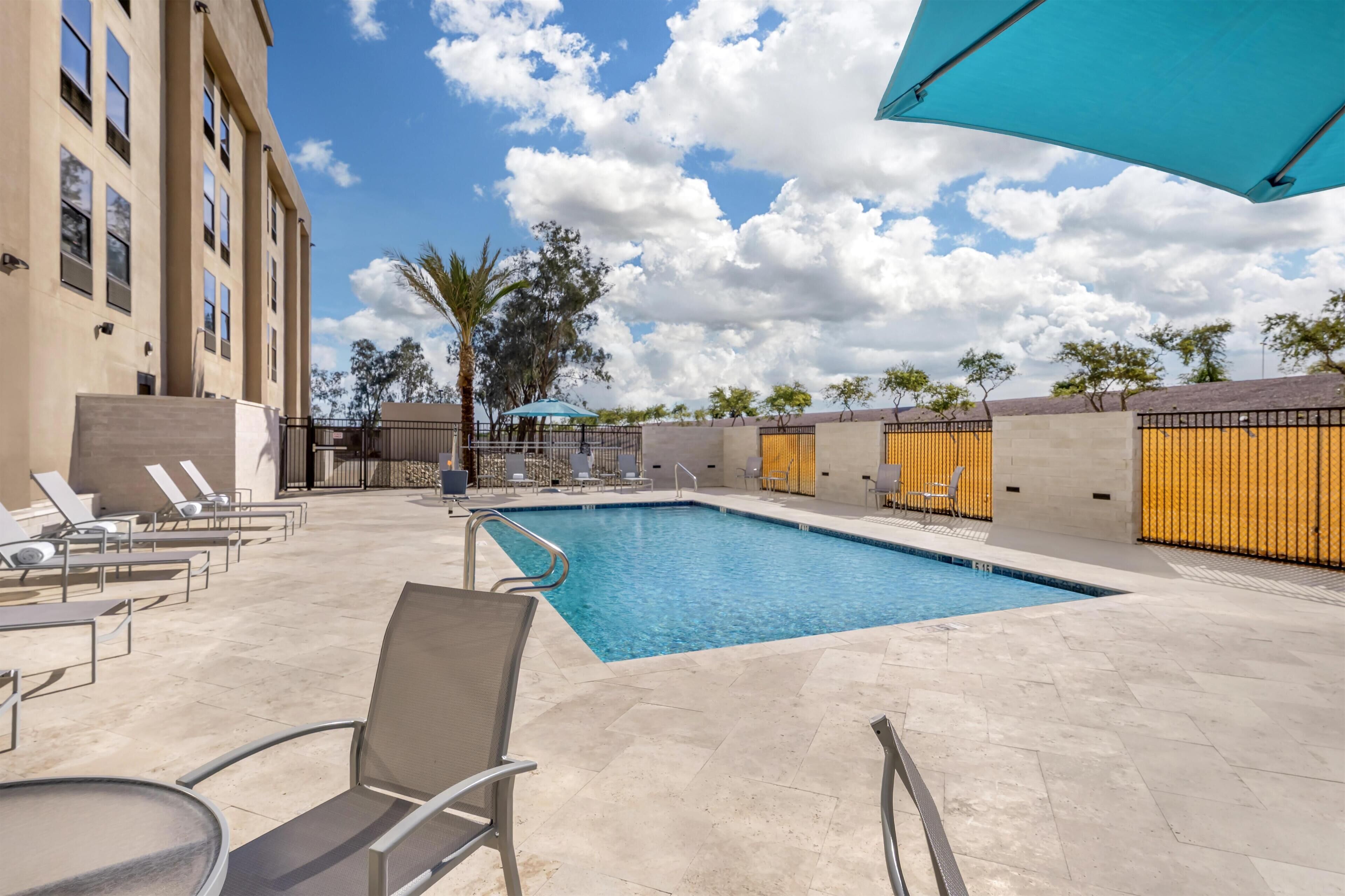 A swimming pool with lounge chairs and a covered area, surrounded by a building with a tiled patio.