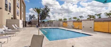A swimming pool with lounge chairs and a covered area, surrounded by a building with a tiled patio.