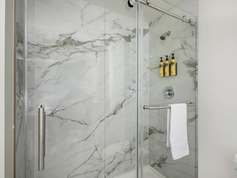 A bathroom with a glass-enclosed shower, marble walls, and a white towel hanging on a rack.