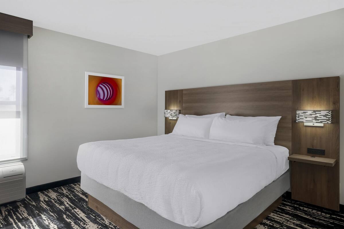 A hotel room with a large bed, a wooden headboard, a wall-mounted light, and a window with curtains.