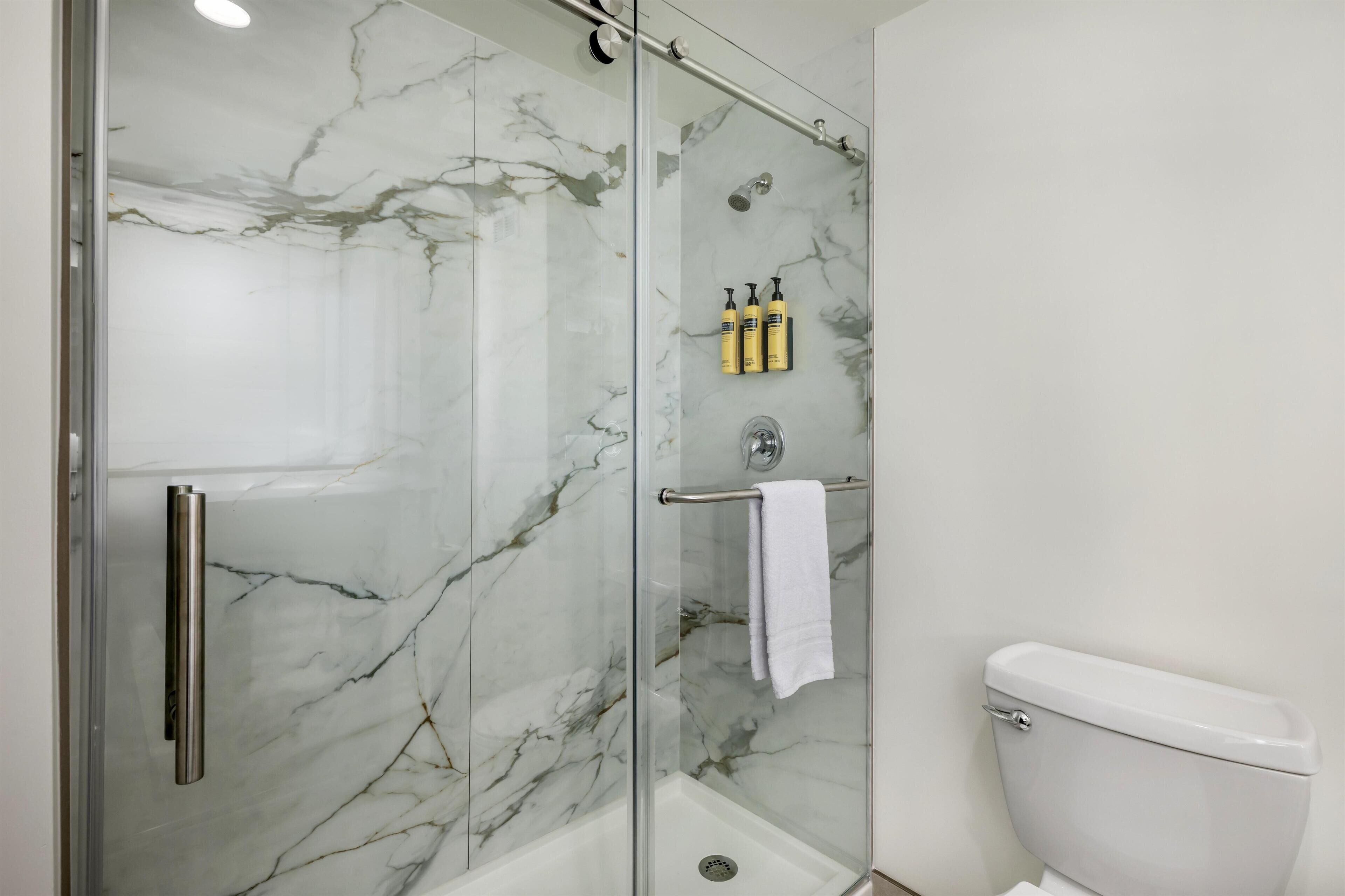 A bathroom with a glass-enclosed shower, a toilet, and a towel rack with a towel.