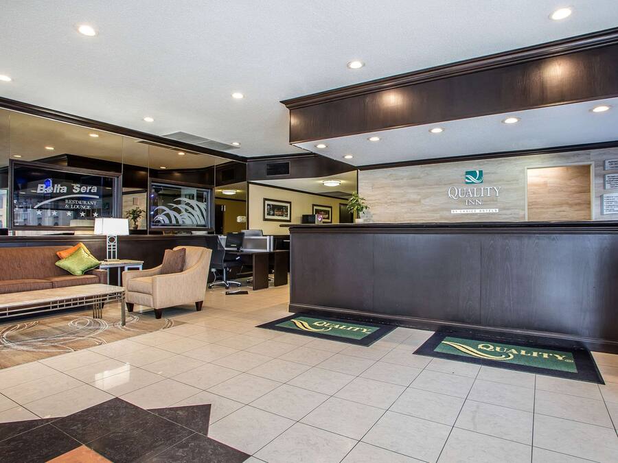 A hotel reception area with a reception desk, a waiting area with a sofa and armchairs, and a television screen displaying the hotel's name.