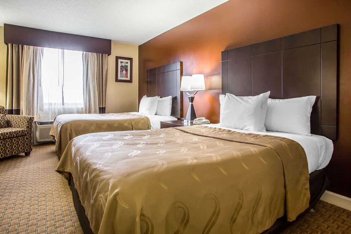 Quarto de hotel com duas camas, um sofá, uma luminária e um quadro na parede.