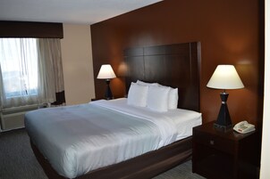 Una habitación de hotel con una cama grande, dos lámparas de noche, un teléfono y una ventana con cortinas.